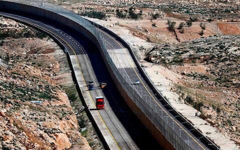 Cars drive on a 2019 Israeli road dividing by a wall to separate the road for Palestinians. Route 4370 has been called the Apartheid Road